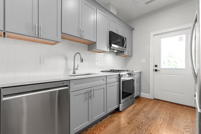 kitchen featuring decorative backsplash, light hardwood / wood-style flooring, sink, gray cabinets, and appliances with stainless steel finishes