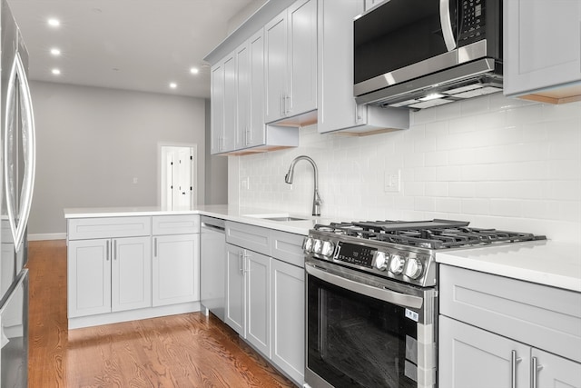 kitchen featuring sink, kitchen peninsula, light hardwood / wood-style floors, stainless steel appliances, and decorative backsplash