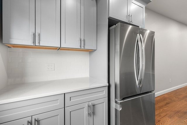 kitchen with dark wood-type flooring, backsplash, stainless steel refrigerator, and gray cabinets