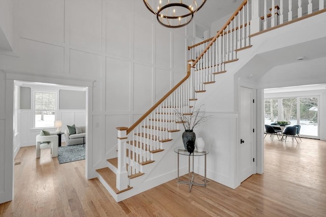 staircase with a notable chandelier, a decorative wall, a high ceiling, and wood finished floors