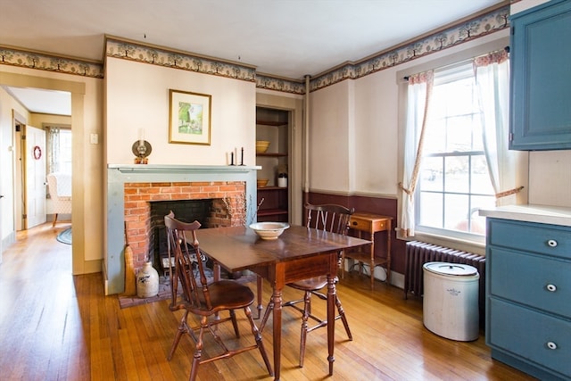 dining room featuring a brick fireplace, light hardwood / wood-style floors, radiator heating unit, and a wealth of natural light