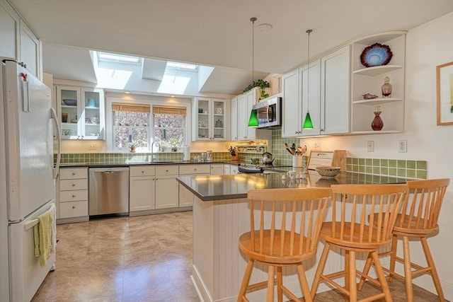 kitchen featuring a peninsula, dark countertops, glass insert cabinets, a skylight, and stainless steel appliances