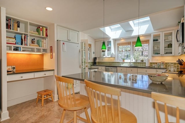 kitchen with stainless steel dishwasher, freestanding refrigerator, open shelves, dark countertops, and a skylight