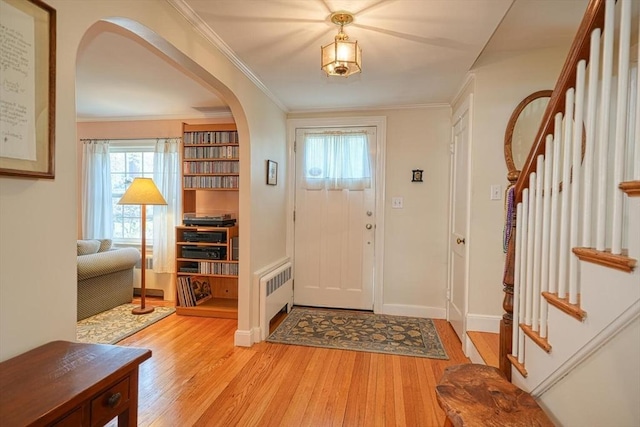 foyer featuring arched walkways, radiator, light wood-style flooring, and stairway