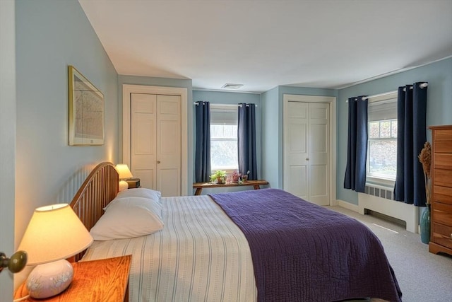 carpeted bedroom with visible vents, baseboards, two closets, and radiator heating unit