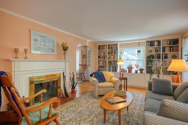 living room with a fireplace, arched walkways, built in shelves, wood finished floors, and ornamental molding