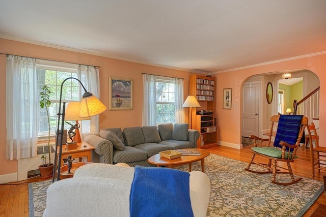 living room with crown molding, arched walkways, baseboards, and wood finished floors