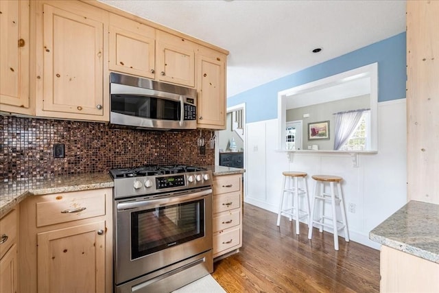 kitchen featuring decorative backsplash, light brown cabinetry, appliances with stainless steel finishes, light stone countertops, and wood finished floors