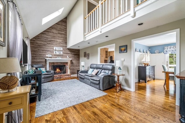 living area with a skylight, high vaulted ceiling, a fireplace, and wood finished floors