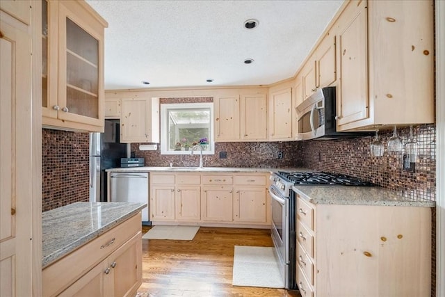 kitchen featuring light brown cabinets, light wood-type flooring, tasteful backsplash, light stone counters, and stainless steel appliances