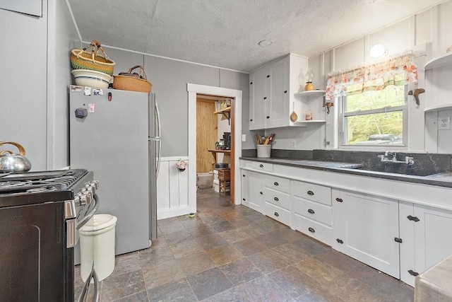 kitchen with appliances with stainless steel finishes, open shelves, a textured ceiling, white cabinetry, and stone finish floors