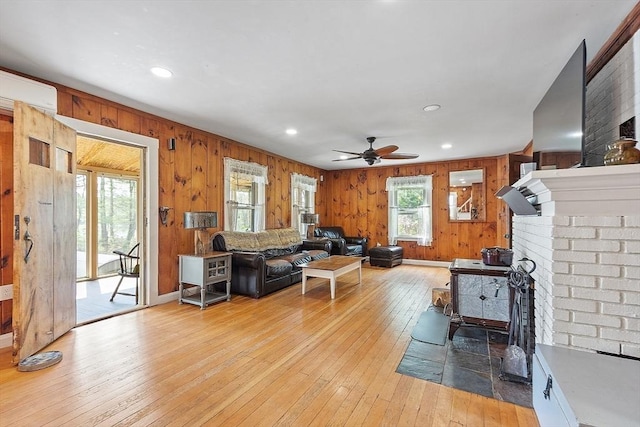 living room featuring light wood finished floors, a ceiling fan, wood walls, recessed lighting, and a brick fireplace