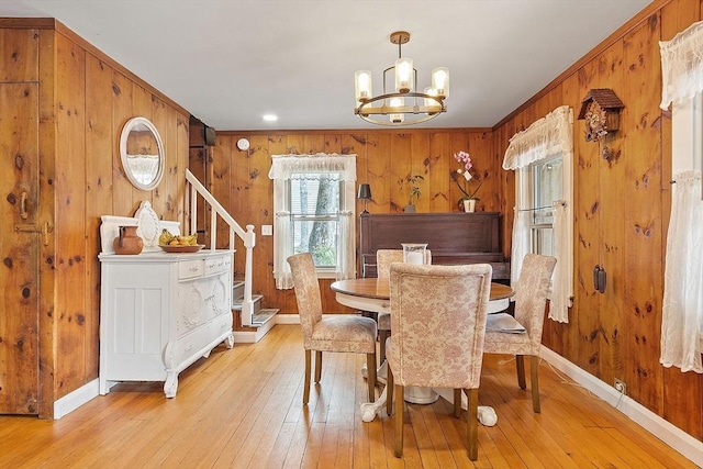 dining room featuring a chandelier, light wood-style floors, wooden walls, baseboards, and stairway