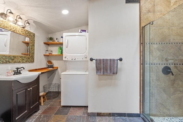 full bathroom featuring stacked washing machine and dryer, a shower stall, vaulted ceiling, vanity, and stone finish flooring