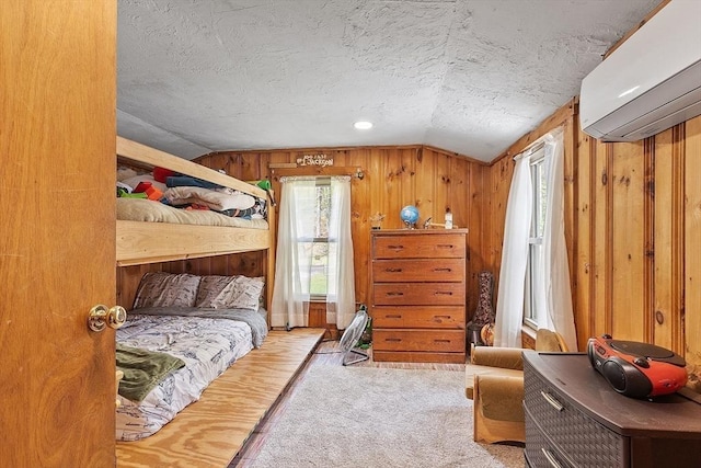 carpeted bedroom with a wall mounted AC, vaulted ceiling, a textured ceiling, and wood walls
