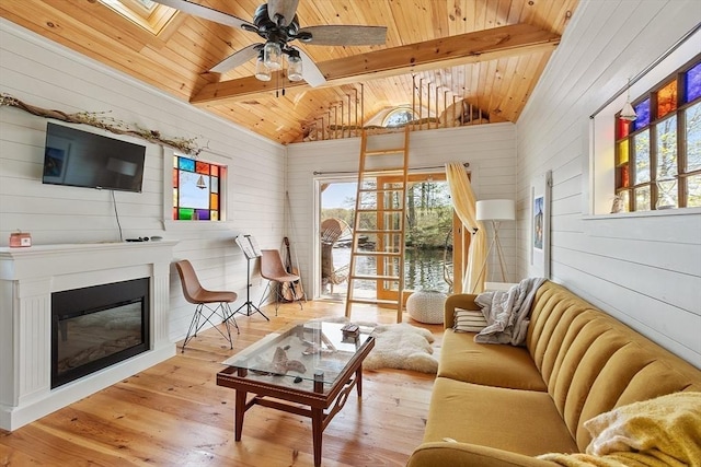 living area featuring wooden walls, wooden ceiling, hardwood / wood-style floors, a glass covered fireplace, and a ceiling fan