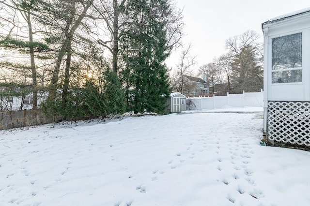 snowy yard featuring a storage unit, fence, and an outbuilding