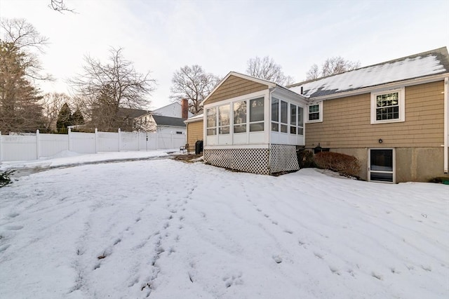 snow covered back of property with a sunroom, fence, and a detached garage