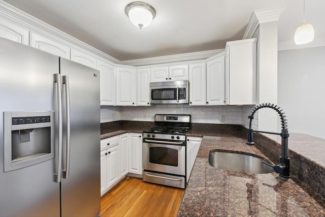 kitchen featuring sink, appliances with stainless steel finishes, white cabinetry, dark stone countertops, and decorative light fixtures