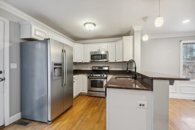 kitchen featuring appliances with stainless steel finishes, decorative light fixtures, white cabinetry, sink, and kitchen peninsula