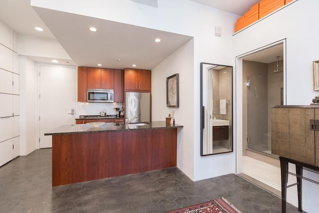 kitchen featuring appliances with stainless steel finishes, dark stone counters, concrete flooring, and a peninsula