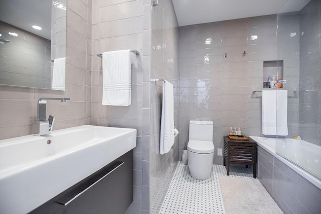 full bath with toilet, tile patterned flooring, tiled shower / bath, vanity, and tile walls