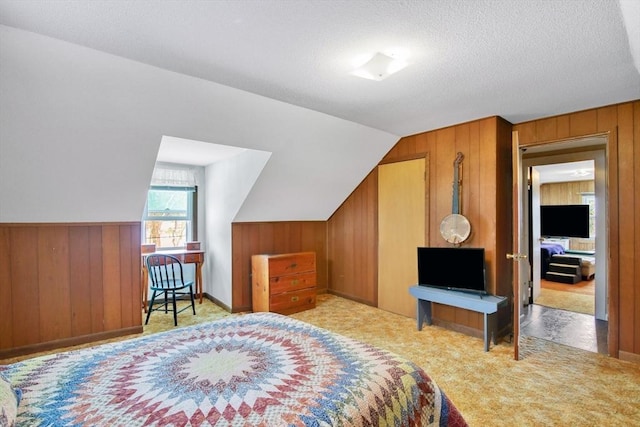 bedroom with wooden walls, light colored carpet, a textured ceiling, and vaulted ceiling