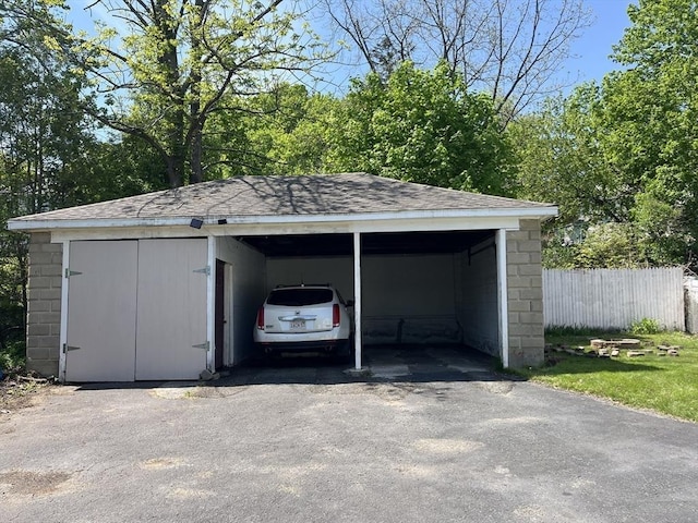 garage with fence, a carport, and asphalt driveway