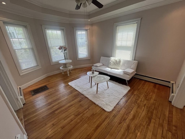 living area featuring crown molding, a tray ceiling, hardwood / wood-style flooring, baseboards, and a ceiling fan