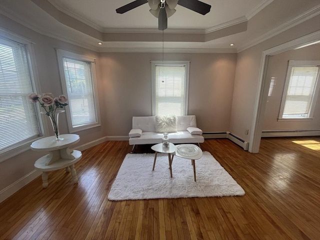 living room with a raised ceiling, hardwood / wood-style flooring, ceiling fan, baseboards, and crown molding