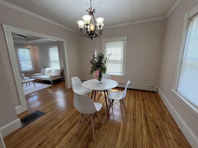 dining area with baseboard heating, a chandelier, wood-type flooring, ornamental molding, and baseboards