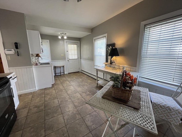 kitchen featuring wainscoting, electric range, baseboard heating, white cabinetry, and stone finish flooring