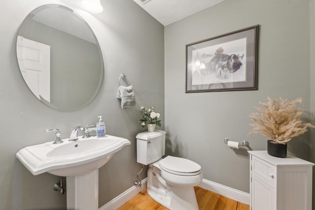 half bathroom with toilet, baseboards, and wood finished floors