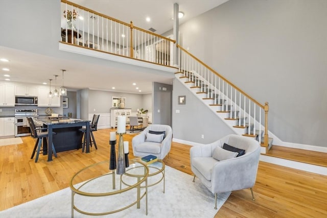 living area with light wood-style floors, recessed lighting, stairs, and a towering ceiling