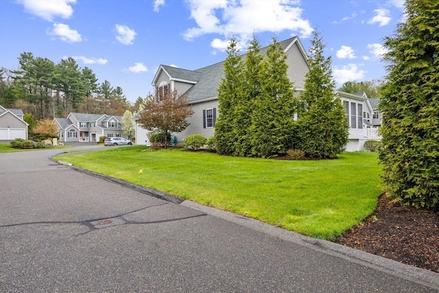 view of property exterior with a residential view, a yard, a garage, and aphalt driveway