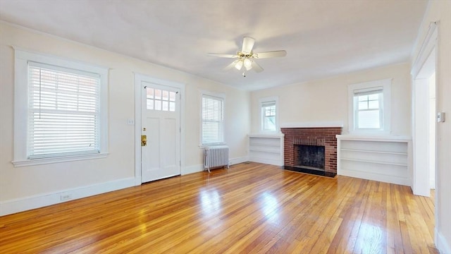 unfurnished living room featuring a brick fireplace, light wood-style flooring, radiator heating unit, and a wealth of natural light