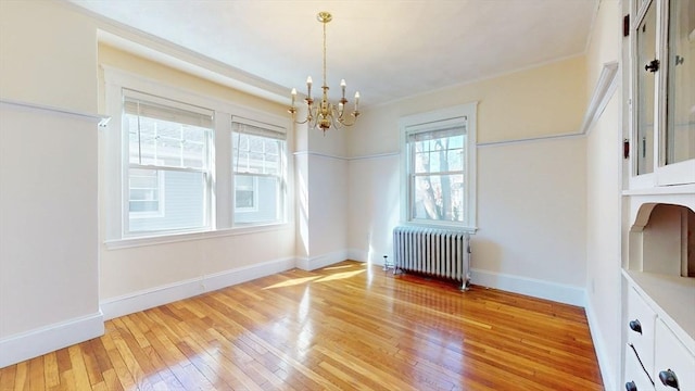 unfurnished dining area featuring baseboards, an inviting chandelier, radiator heating unit, ornamental molding, and light wood-type flooring