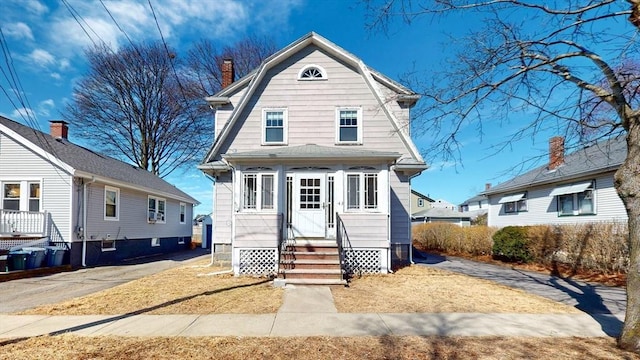 view of front of property featuring entry steps, a gambrel roof, and a chimney