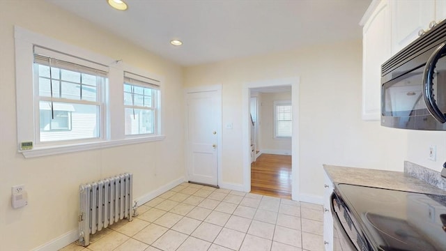 kitchen with radiator heating unit, white cabinets, black microwave, range with electric stovetop, and a wealth of natural light