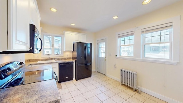 kitchen with black appliances, radiator heating unit, white cabinets, light countertops, and a healthy amount of sunlight