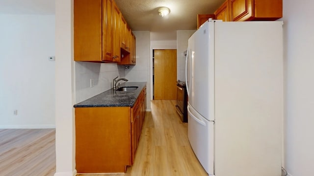 kitchen with decorative backsplash, light hardwood / wood-style floors, white refrigerator, a textured ceiling, and sink