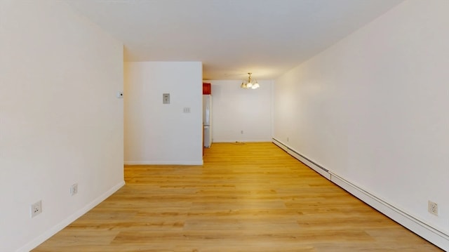 spare room featuring light wood-type flooring, a baseboard heating unit, and a notable chandelier