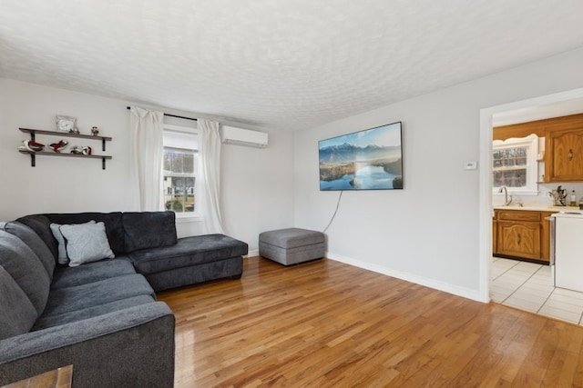 living room with a wall mounted air conditioner, a wealth of natural light, a textured ceiling, and light hardwood / wood-style floors