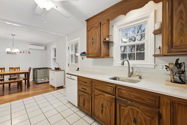 kitchen featuring light tile patterned flooring, sink, decorative light fixtures, an AC wall unit, and white dishwasher