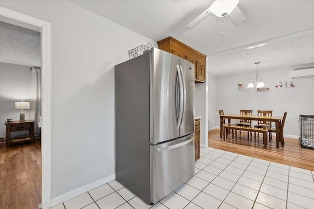 kitchen with light tile patterned flooring, hanging light fixtures, an AC wall unit, stainless steel fridge, and ceiling fan with notable chandelier