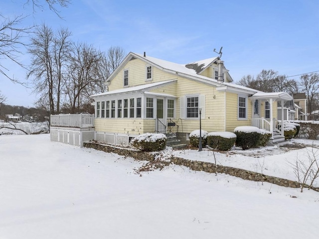 snow covered back of property with a sunroom