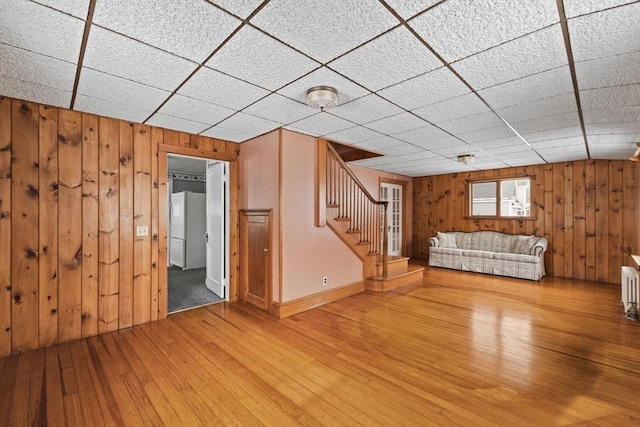 unfurnished living room with radiator, hardwood / wood-style floors, wooden walls, and a drop ceiling