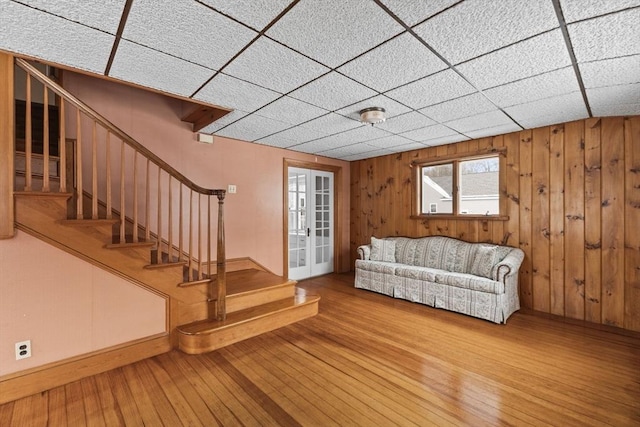 unfurnished living room with wood-type flooring, a drop ceiling, wood walls, and french doors