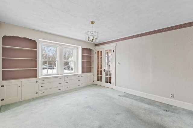 spare room featuring french doors, light carpet, and a notable chandelier