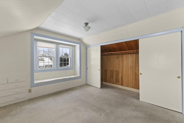 unfurnished bedroom with wooden walls, light colored carpet, a closet, and lofted ceiling